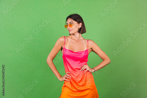 Stylish woman in pink silk dress isolated on green background posing, perfect curves, slender, tanned © Анастасия Каргаполов