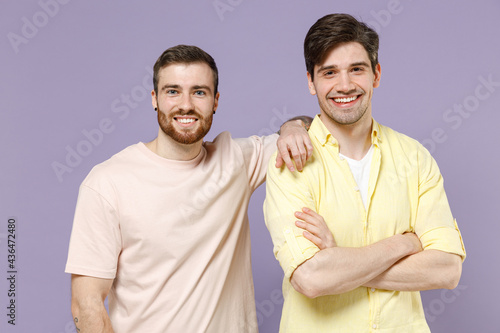 Two young happy positive cool smiling men friends together in casual t-shirt hug leaning each other hold hands crossed folded isolated on purple background studio portrait People lifestyle concept