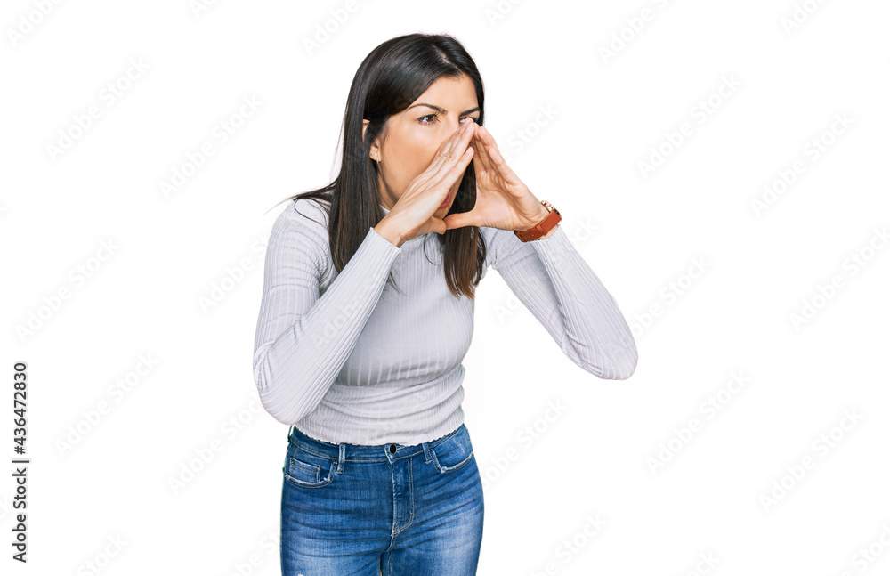 Beautiful brunette woman wearing casual clothes shouting angry out loud with hands over mouth Beautiful brunette woman wearing casual clothes shouting angry out loud with hands over mouth