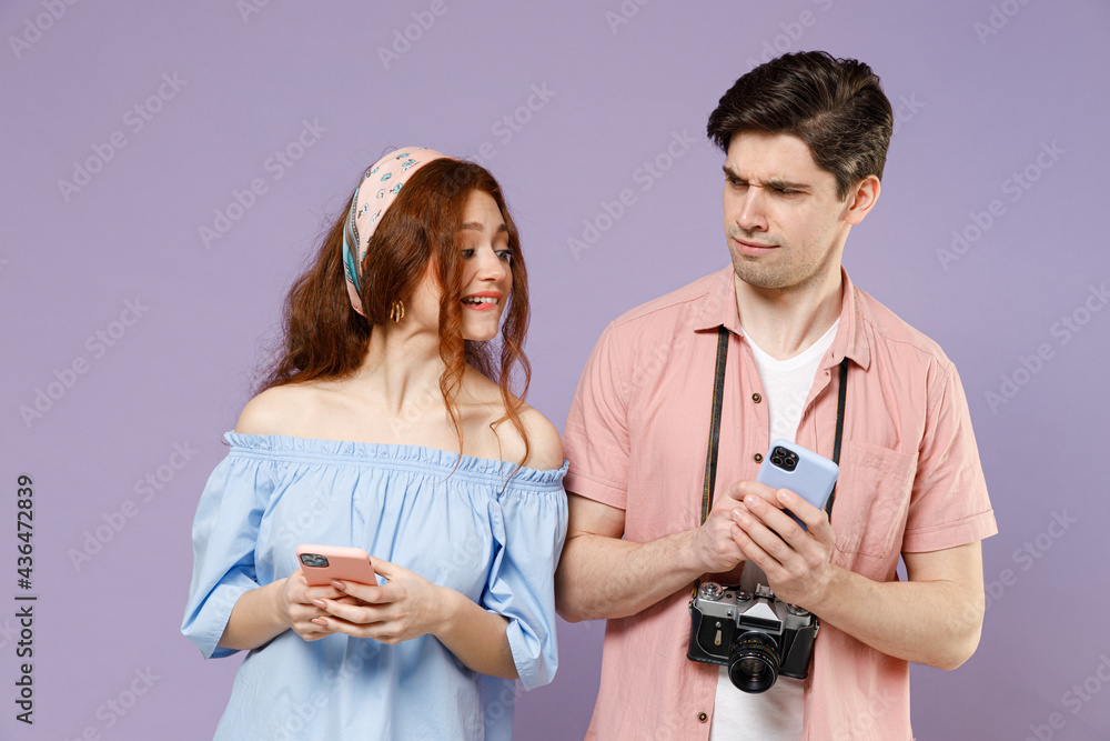 Two indignant traveler tourist woman man couple in casual clothes use hold mobile cell phone peep isolated on purple background. Passenger travel abroad weekend getaway. Air flight journey concept Two indignant traveler tourist woman man couple in casual clothes use hold mobile cell phone peep isolated on purple background. Passenger travel abroad weekend getaway. Air flight journey concept