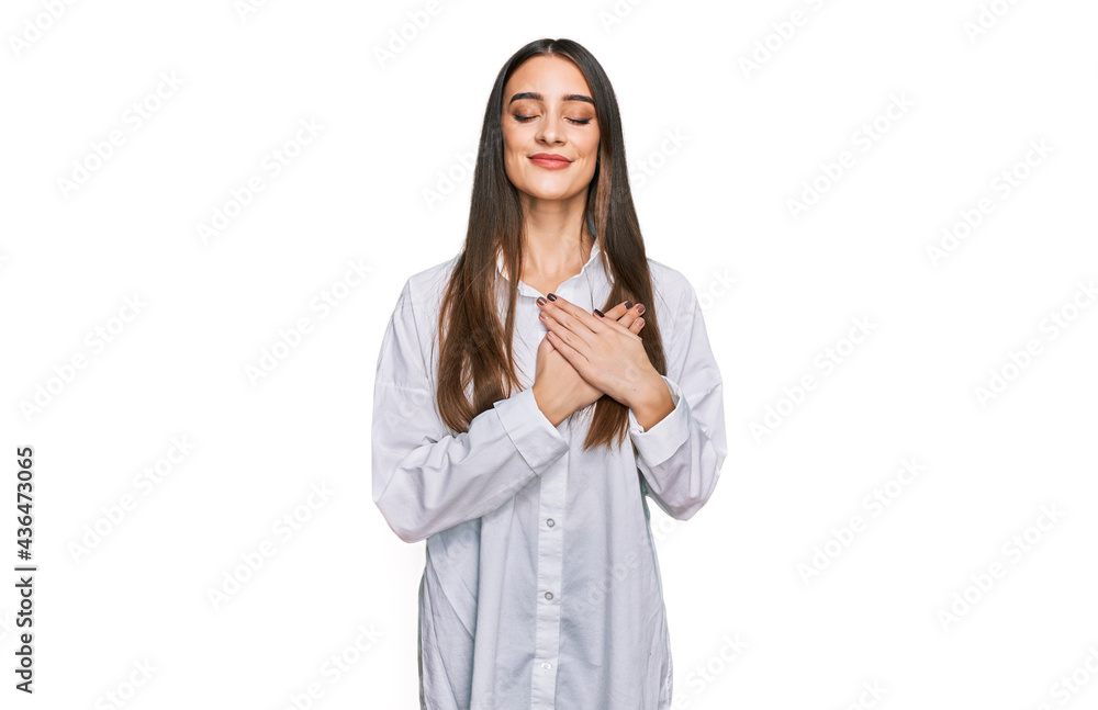 Young beautiful woman wearing casual white shirt smiling with hands on chest with closed eyes and grateful gesture on face. health concept. Young beautiful woman wearing casual white shirt smiling with hands on chest with closed eyes and grateful gesture on face. health concept.
