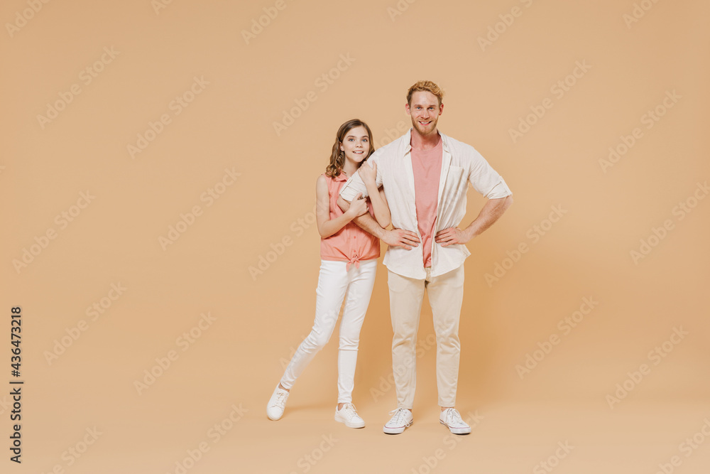 Full length happy young parent man with child teen girl in casual pastel clothes. Daddy little kid daughter stand akimbo hands on waist isolated on beige background. Father's Day Love family concept. Full length happy young parent man with child teen girl in casual pastel clothes. Daddy little kid daughter stand akimbo hands on waist isolated on beige background. Father's Day Love family concept.