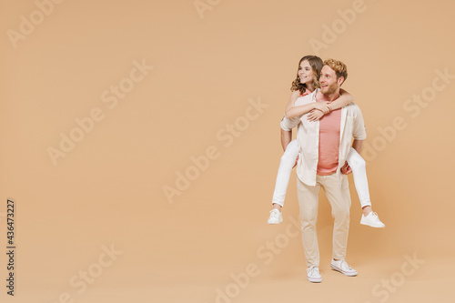 Full length young parent man, child teen girl in casual clothes Dad little kid daughter give piggyback ride joyful sit on back look aside isolated on beige background Father's Day Love family concept.