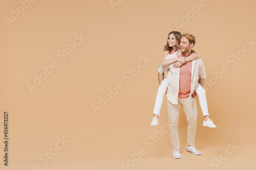 Fototapeta Full length young parent man, child teen girl in casual clothes Dad little kid daughter give piggyback ride joyful sit on back look aside isolated on beige background Father's Day Love family concept