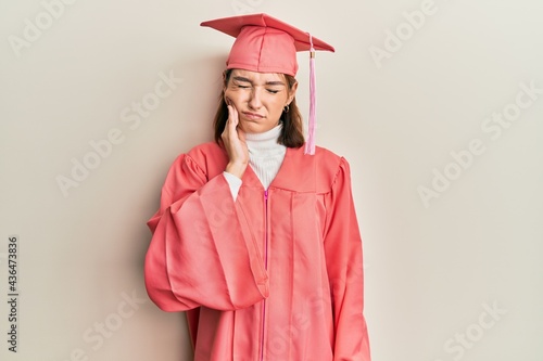 Young caucasian woman wearing graduation cap and ceremony robe touching mouth with hand with painful expression because of toothache or dental illness on teeth. dentist