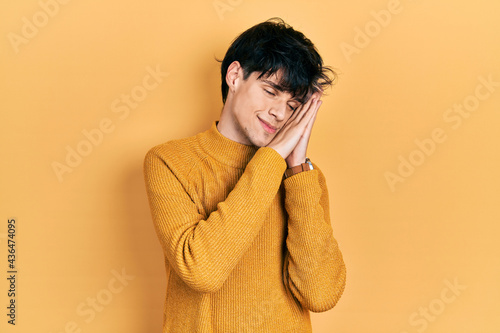 Handsome hipster young man wearing casual yellow sweater sleeping tired dreaming and posing with hands together while smiling with closed eyes.