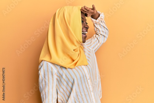 Beautiful african young woman wearing traditional islamic hijab scarf very happy and smiling looking far away with hand over head. searching concept.