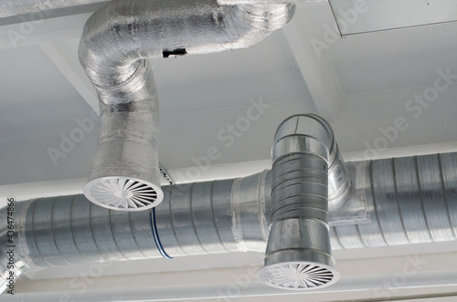 Air duct, air conditioner pipe on white ceiling wall. Ventilation system on the ceiling of large building. Ventilation pipes in silver insulation material hanging from the ceiling inside new building.