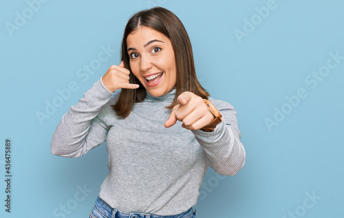 Foto Young beautiful woman wearing casual turtleneck sweater smiling doing talking on the telephone gesture and pointing to you