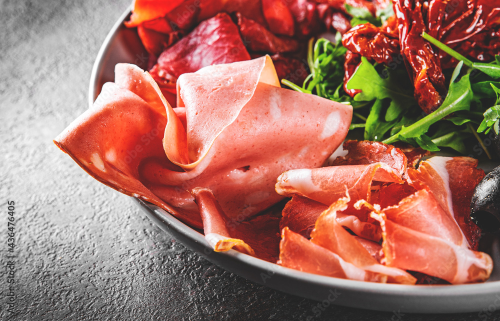 plate with meat, salami, ham, backon, prosciutto on Dark grey black slate background