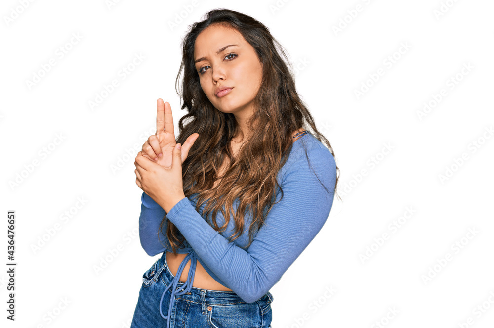 Young hispanic girl wearing casual clothes holding symbolic gun with hand gesture, playing killing shooting weapons, angry face Young hispanic girl wearing casual clothes holding symbolic gun with hand gesture, playing killing shooting weapons, angry face