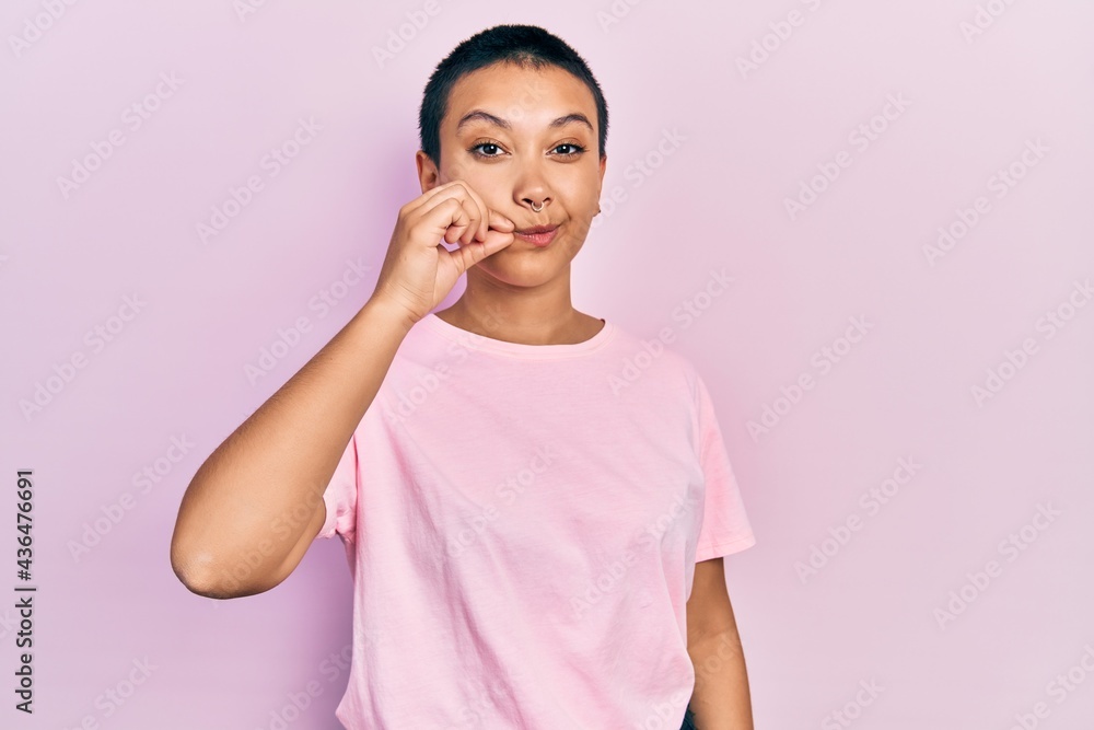 Beautiful hispanic woman with short hair wearing casual pink t shirt mouth and lips shut as zip with fingers. secret and silent, taboo talking Beautiful hispanic woman with short hair wearing casual pink t shirt mouth and lips shut as zip with fingers. secret and silent, taboo talking
