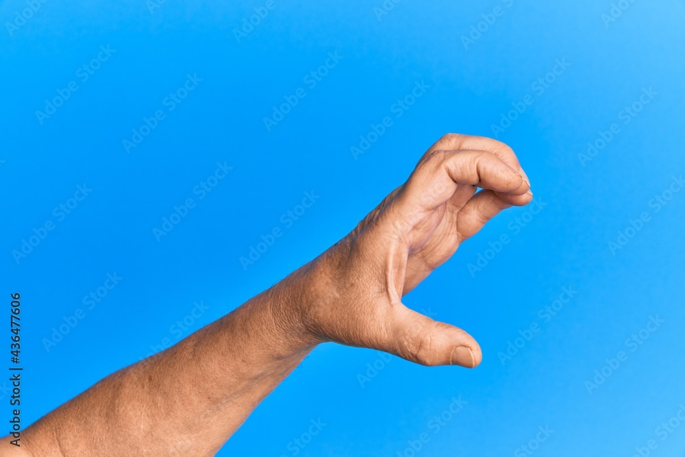 Hand of senior hispanic man over blue isolated background picking and taking invisible thing, holding object with fingers showing space Hand of senior hispanic man over blue isolated background picking and taking invisible thing, holding object with fingers showing space