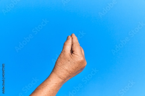 Hand of senior hispanic man over blue isolated background holding blank space with thumb finger, business and advertising