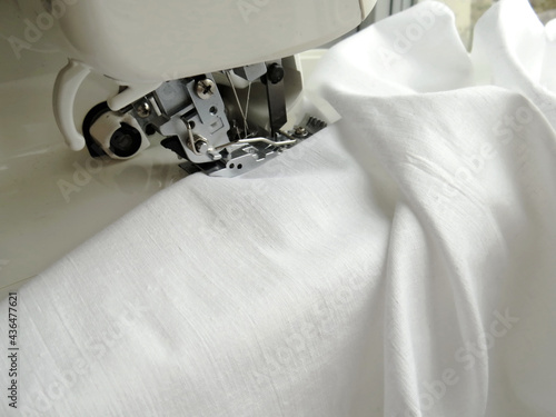 The sewing machine is sewing white fabric. Overlock fabric edges. Garment industry photo