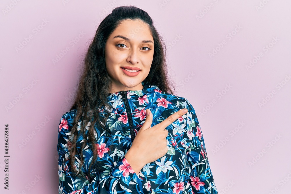 Beautiful middle eastern woman wearing casual floral jacket cheerful with a smile of face pointing with hand and finger up to the side with happy and natural expression on face Beautiful middle eastern woman wearing casual floral jacket cheerful with a smile of face pointing with hand and finger up to the side with happy and natural expression on face