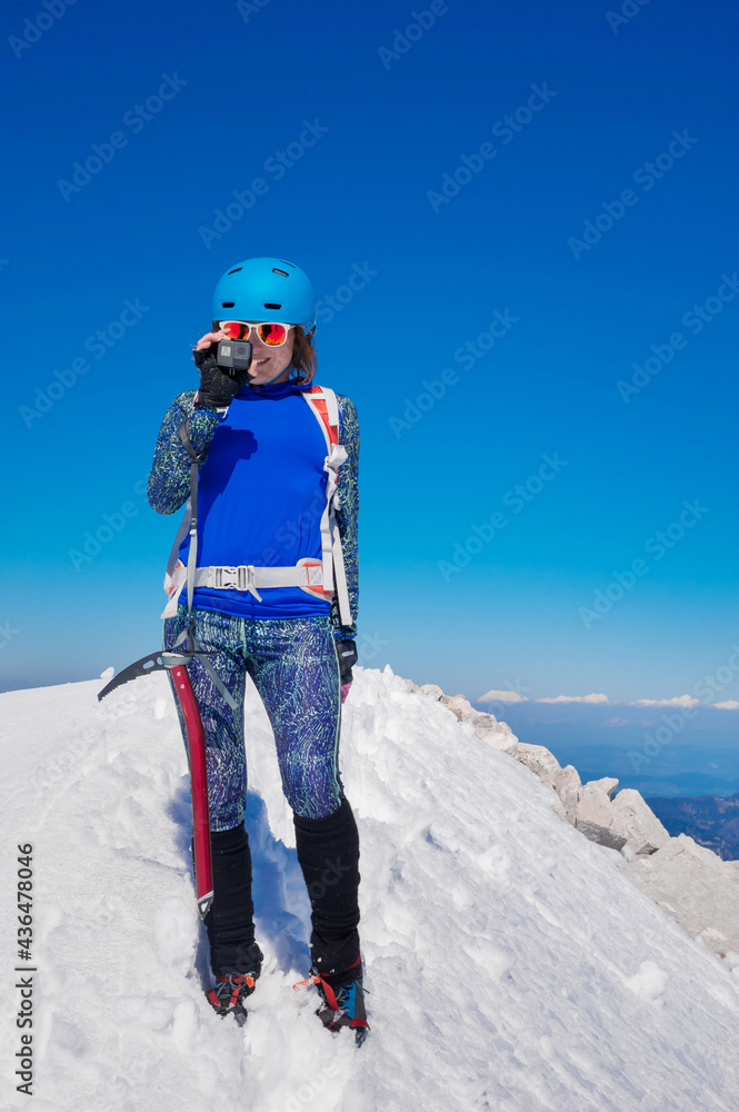 beautiful sporty girl climber takes photos on a small camera from the top of the conquered peak 