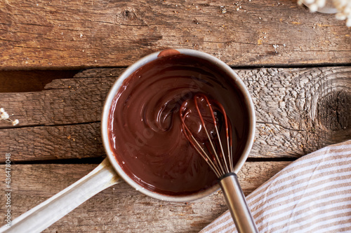 chocolate ganache in a saucepan with a whisk. Top view, wooden background.