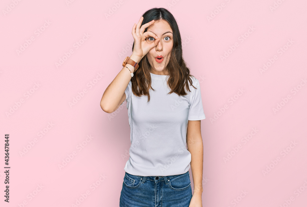 Young beautiful woman wearing casual white t shirt doing ok gesture shocked with surprised face, eye looking through fingers. unbelieving expression. Young beautiful woman wearing casual white t shirt doing ok gesture shocked with surprised face, eye looking through fingers. unbelieving expression.
