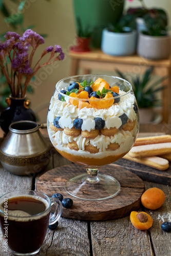 Apricot trifle with blueberries, cookies and cream cheese. Wooden background, side view