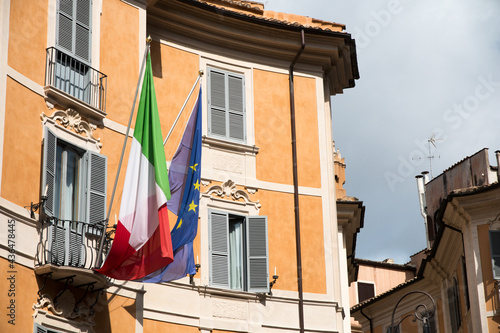 Italian flag and European flag waving in the air hanging on a balkony in Italy.