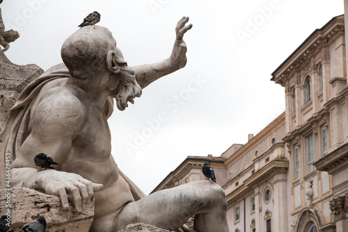 Stone statue of a man with his hand dramatically in the air with pigeons on its body. Details of statue Piazza navona square, rome, Italy.