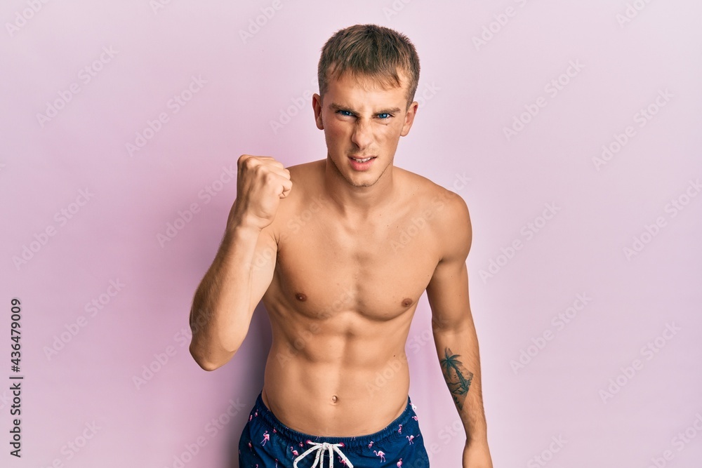 Young caucasian man wearing swimwear angry and mad raising fist frustrated and furious while shouting with anger. rage and aggressive concept. Young caucasian man wearing swimwear angry and mad raising fist frustrated and furious while shouting with anger. rage and aggressive concept.