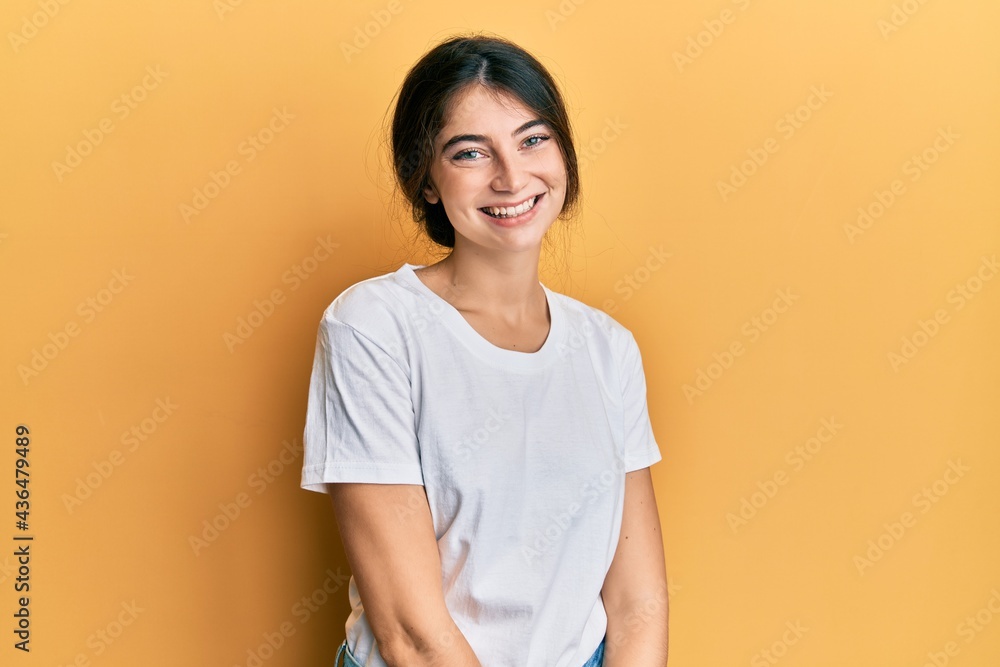 Young caucasian woman wearing casual white t shirt looking positive and happy standing and smiling with a confident smile showing teeth Young caucasian woman wearing casual white t shirt looking positive and happy standing and smiling with a confident smile showing teeth