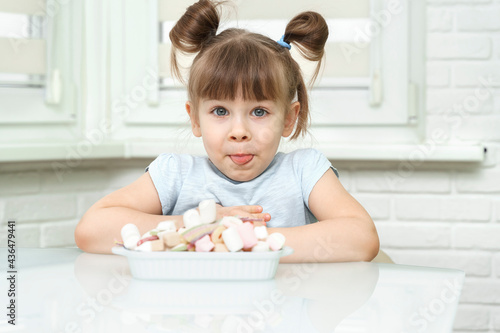 happy contented little girl eating marshmallows from a plate full of sweets. the child is addicted to sugar