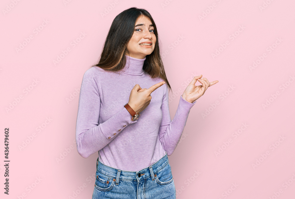 Young beautiful teen girl wearing turtleneck sweater pointing aside worried and nervous with both hands, concerned and surprised expression