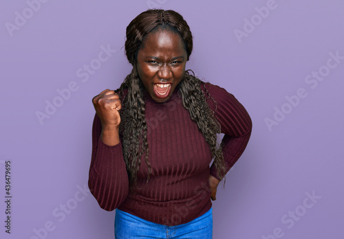 Young african woman wearing casual winter sweater angry and mad raising fist frustrated and furious while shouting with anger. rage and aggressive concept.