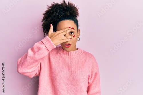 Young african american girl wearing casual clothes peeking in shock covering face and eyes with hand, looking through fingers afraid © Krakenimages.com