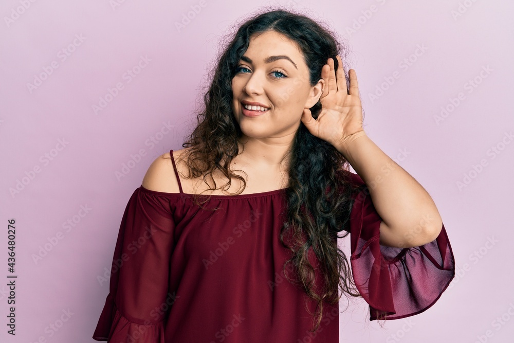 Young brunette woman with curly hair wearing casual clothes smiling with hand over ear listening and hearing to rumor or gossip. deafness concept. Young brunette woman with curly hair wearing casual clothes smiling with hand over ear listening and hearing to rumor or gossip. deafness concept.