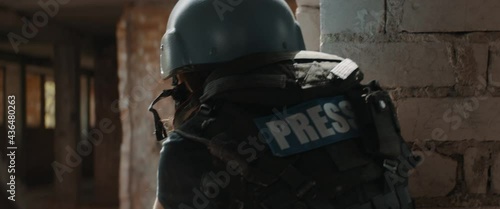 Caucasian female war journalist wearing protective helmet and bulletproof vest gear taking photos during military operation. Shot with 2x anamorphic lens photo