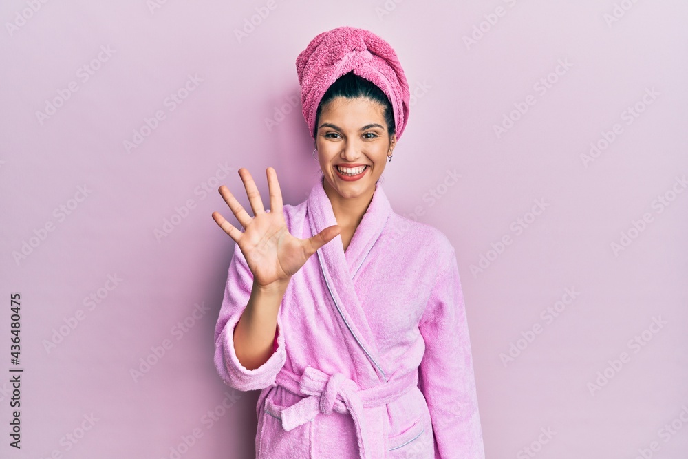 Young hispanic woman wearing shower towel cap and bathrobe showing and pointing up with fingers number five while smiling confident and happy. Young hispanic woman wearing shower towel cap and bathrobe showing and pointing up with fingers number five while smiling confident and happy.