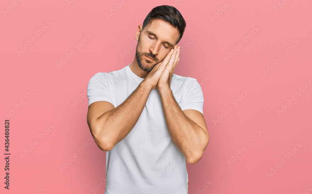 Handsome man with beard wearing casual white t shirt sleeping tired dreaming and posing with hands together while smiling with closed eyes. Handsome man with beard wearing casual white t shirt sleeping tired dreaming and posing with hands together while smiling with closed eyes.