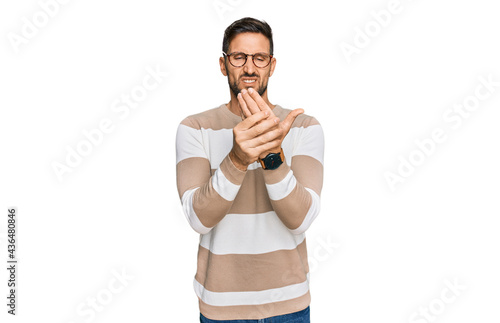 Handsome man with beard wearing casual clothes and glasses suffering pain on hands and fingers, arthritis inflammation