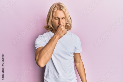 Caucasian young man with long hair wearing casual white t shirt feeling unwell and coughing as symptom for cold or bronchitis. health care concept.