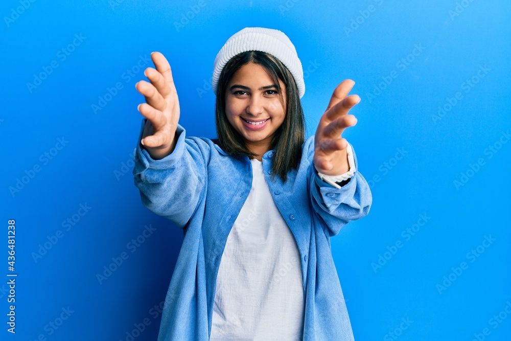 Young latin woman wearing cute wool cap looking at the camera smiling with open arms for hug. cheerful expression embracing happiness. Young latin woman wearing cute wool cap looking at the camera smiling with open arms for hug. cheerful expression embracing happiness.