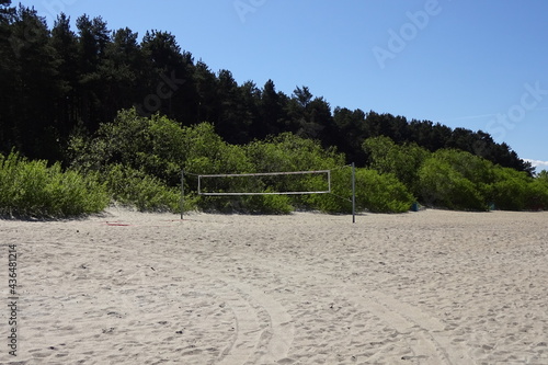 An empty volleyball court on Pirita beach in Tallinn, Estonia. Volleyball net on the beach on a sunny summer day. Green pine trees on the back.