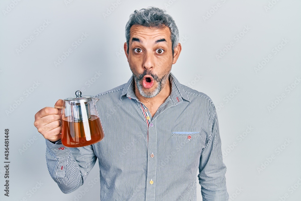 Handsome middle age man with grey hair holding traditional tea pot scared and amazed with open mouth for surprise, disbelief face Handsome middle age man with grey hair holding traditional tea pot scared and amazed with open mouth for surprise, disbelief face