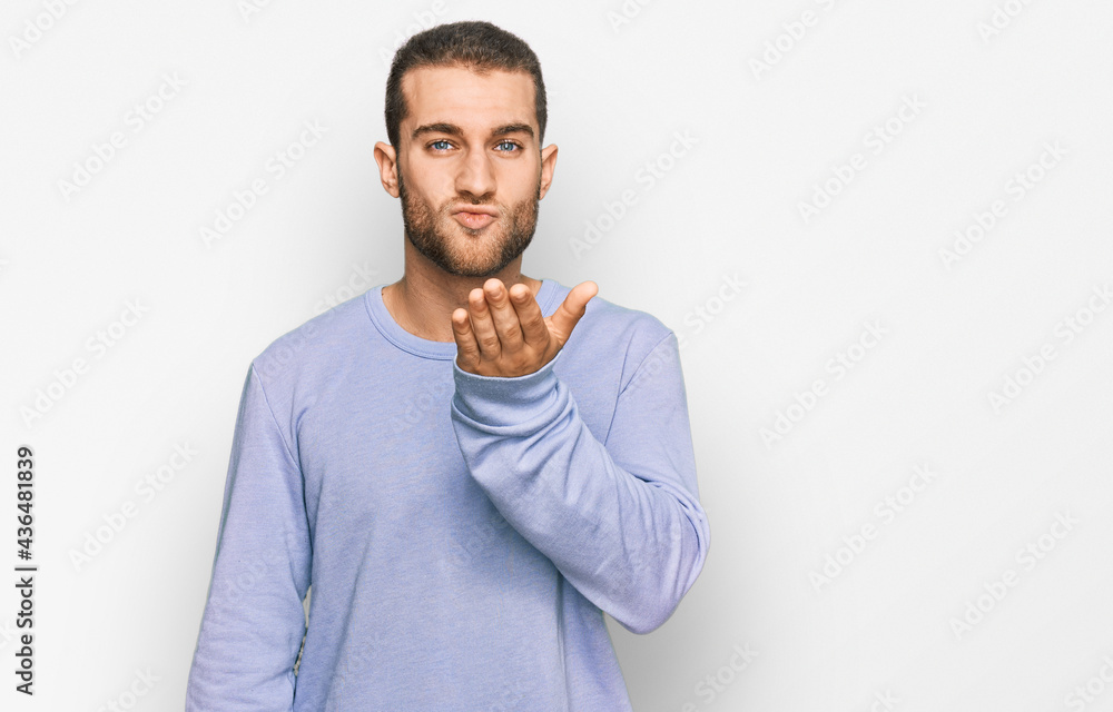 Young caucasian man wearing casual clothes looking at the camera blowing a kiss with hand on air being lovely and sexy. love expression. Young caucasian man wearing casual clothes looking at the camera blowing a kiss with hand on air being lovely and sexy. love expression.