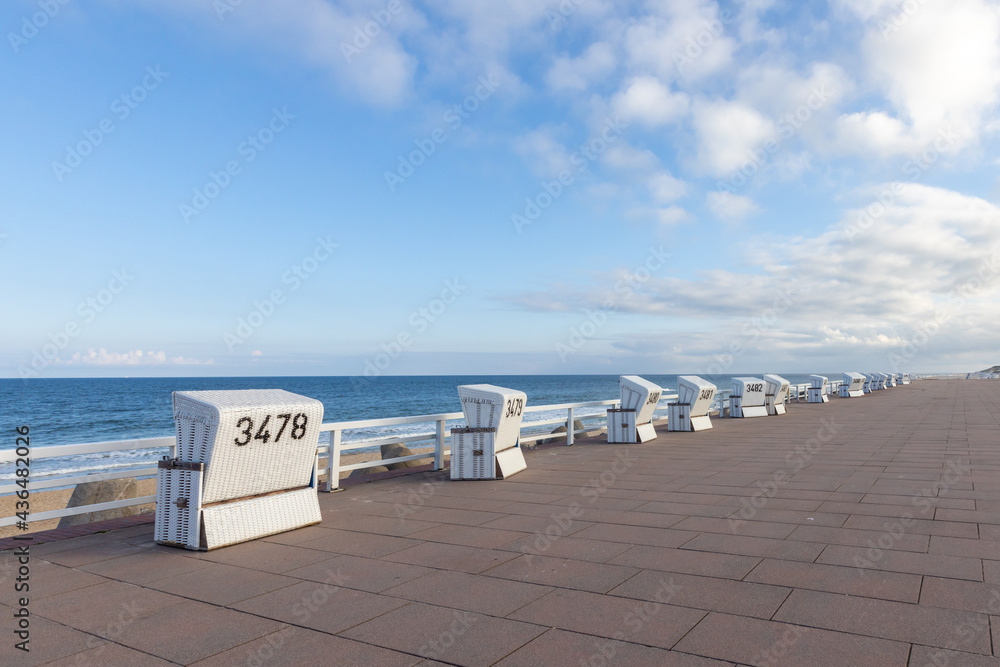 an empty promenade leading along a sea. empty beach chairs in front of a blue sky with the north sea in the background. 