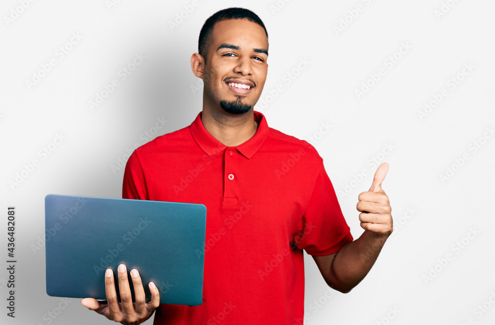 Young african american man working using computer laptop smiling happy and positive, thumb up doing excellent and approval sign Young african american man working using computer laptop smiling happy and positive, thumb up doing excellent and approval sign