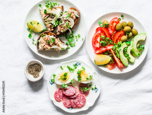 Snack, appetizers, tapas, breakfast table - salami, mackerel cream cheese sandwiches, olives, avocado, tomatoes, micro greens on a light background, top view