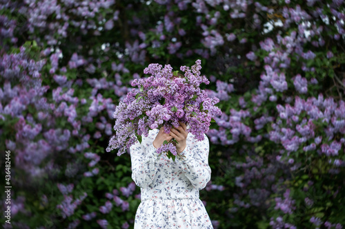Print op canvas Beautiful woman in a dress covers her face with a purple bouquet of Lilacs
