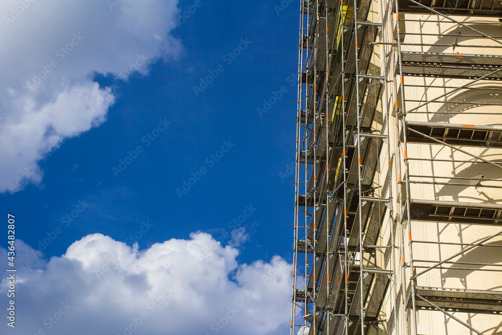 Scaffolding on a high building against the background of a blue summer sky with clouds. Scaffolding on a high building against the background of a blue summer sky with clouds.