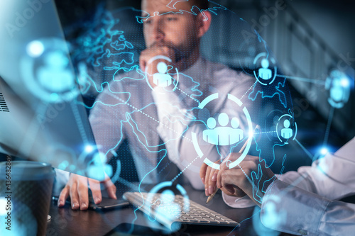 Two colleagues in formal wear working together looking for new employees to hire for international business consulting. HR, social media icons over modern office background