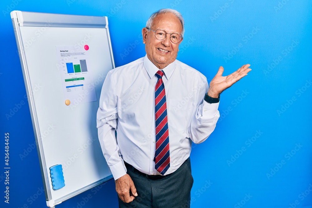 Senior man with grey hair standing by business blackboard smiling cheerful presenting and pointing with palm of hand looking at the camera. Senior man with grey hair standing by business blackboard smiling cheerful presenting and pointing with palm of hand looking at the camera.