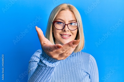 Young blonde woman wearing casual clothes and glasses smiling friendly offering handshake as greeting and welcoming. successful business.